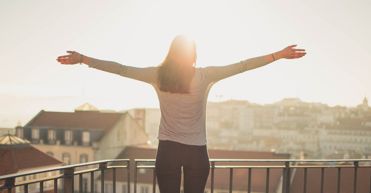 creative-02 A woman stands with outstretched arms on a sunny balcony, embracing the morning light.