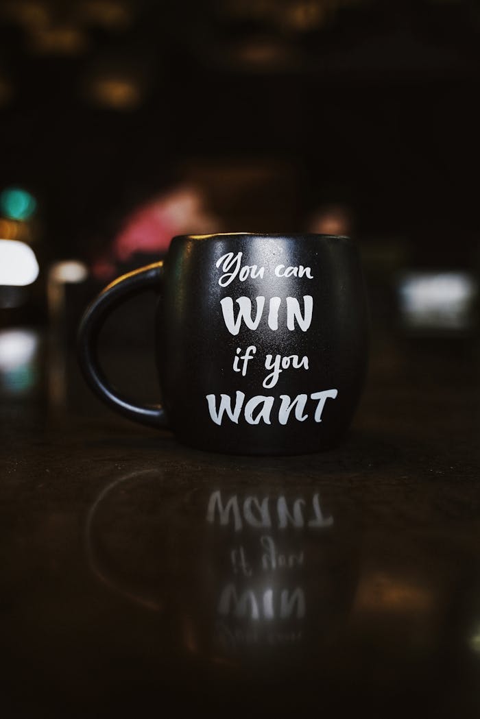 creative-02 Black mug with inspirational quote 'You can win if you want' reflected on a dark surface, creating a motivational ambiance.