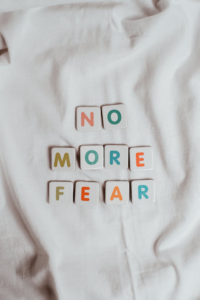 creative-01 Colorful letter tiles spelling 'No More Fear' placed on a soft white fabric background.